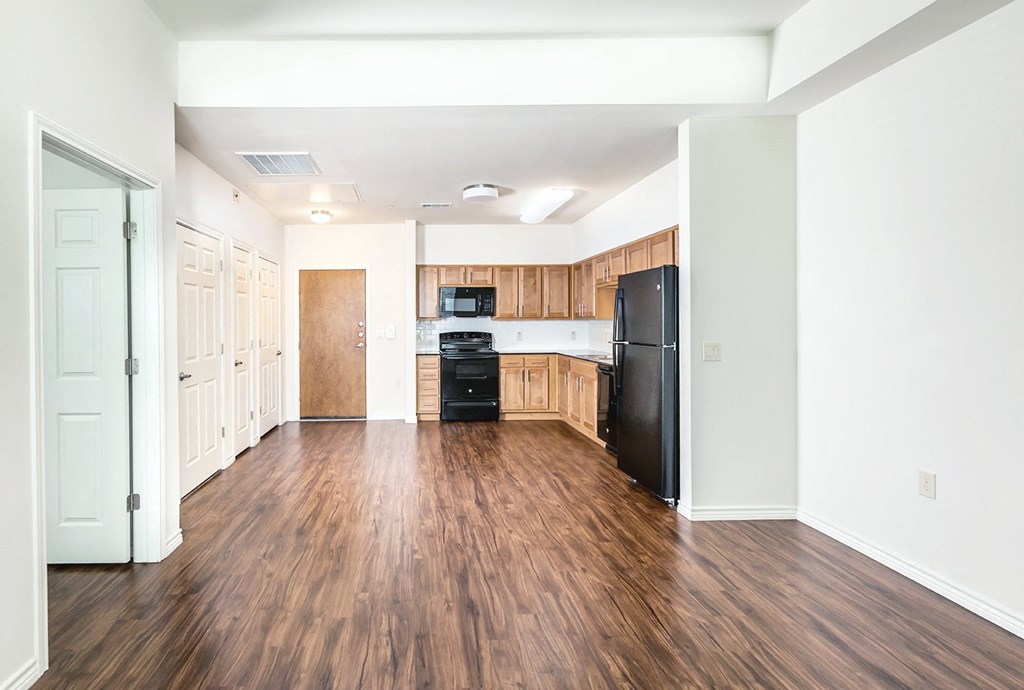 an empty kitchen with wood flooring and a black refrigerator