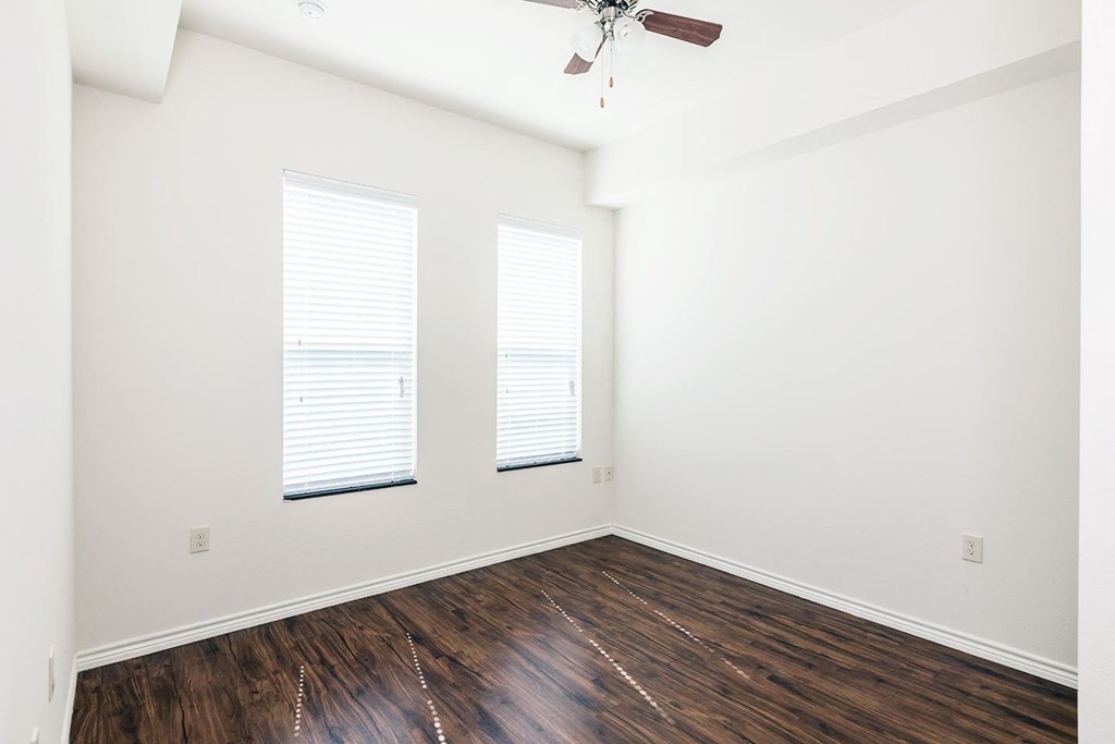 a bedroom with white walls and wood flooring and two windows
