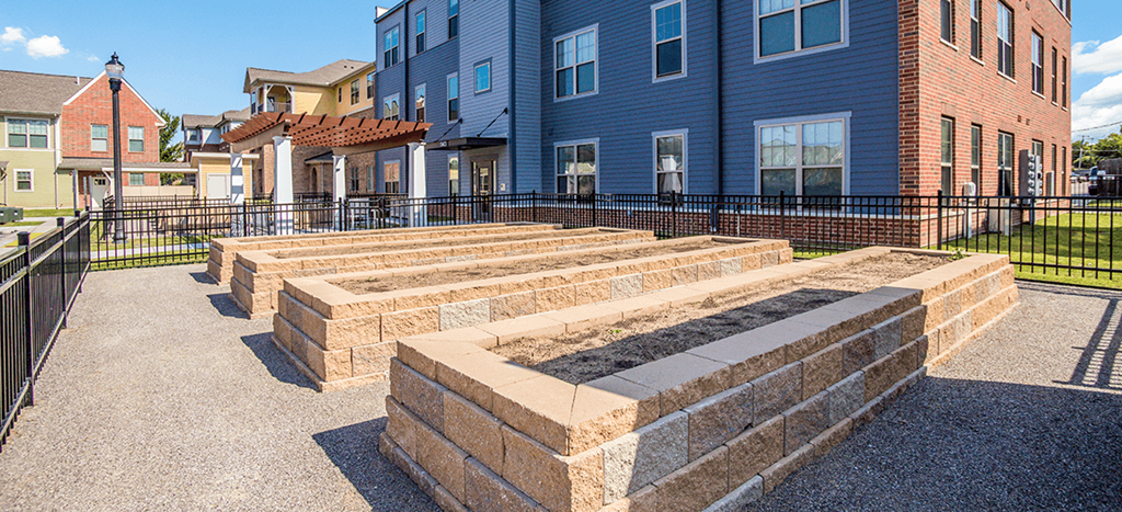 West Park Apartments community garden within a black metal fence sit four cinderblock planters