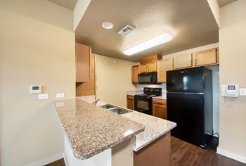 a kitchen with granite countertops and a black refrigerator at Wheatley Park Senior Living San Antonio