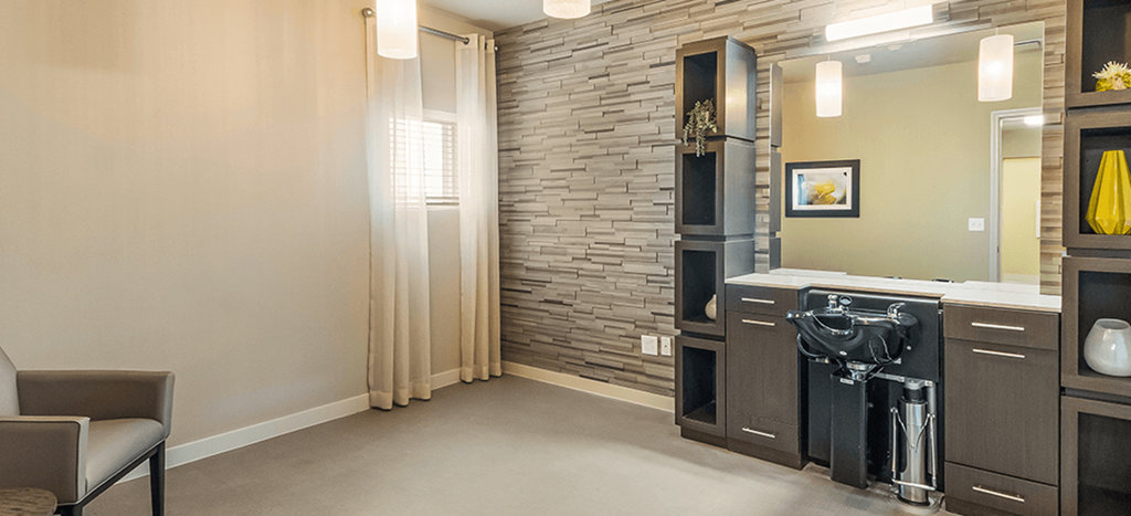 A solon at Wheatley Park Senior Living Apartments with a large mirror, seating and a sink