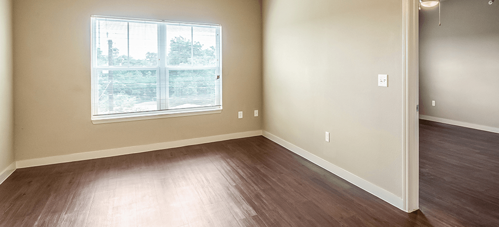 an empty bedroom with wood floors and a window at Wheatley Park Senior Living Apartments