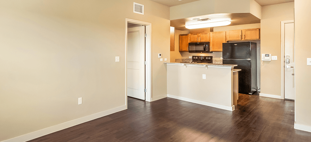 an empty living room and kitchen with wood floors and a black refrigerator at Wheatley Park Senior Living Apartments