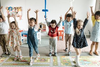 a group of children standing in a classroom with their hands in the air