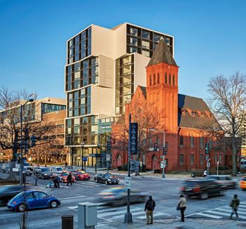 A busy street scene with cars and pedestrians in front of a modern building and a historic church.