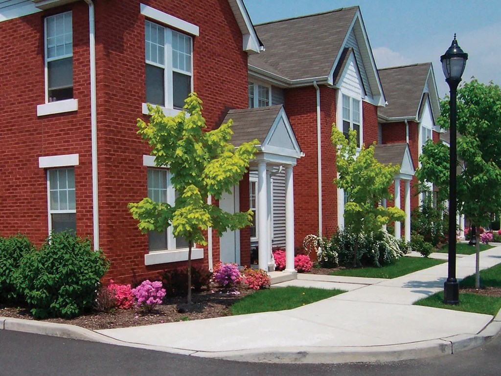 A row of red brick houses with green trees and bushes in front.