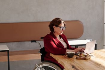 A woman in a red blazer is working on her laptop while sitting in a wheelchair.