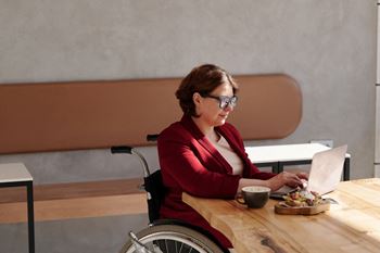 a woman in a wheelchair sitting at a table with a laptop