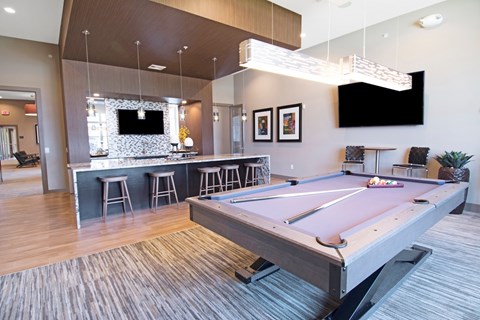 A pool table is in the middle of a room with a bar and a television.