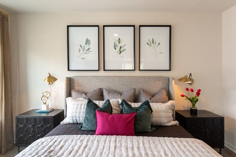 A bed with a grey headboard and a white comforter with a pink pillow in the middle.