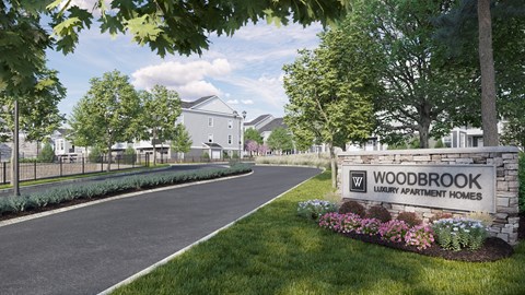 A sign for Woodbrook Luxury Apartment Homes is in the foreground of a well-maintained lawn.