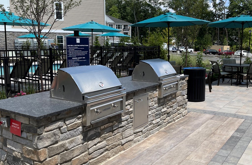 two bbq grills on a stone wall with umbrellas in the background