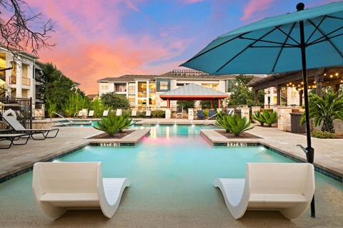 a swimming pool with two white chairs and an umbrella