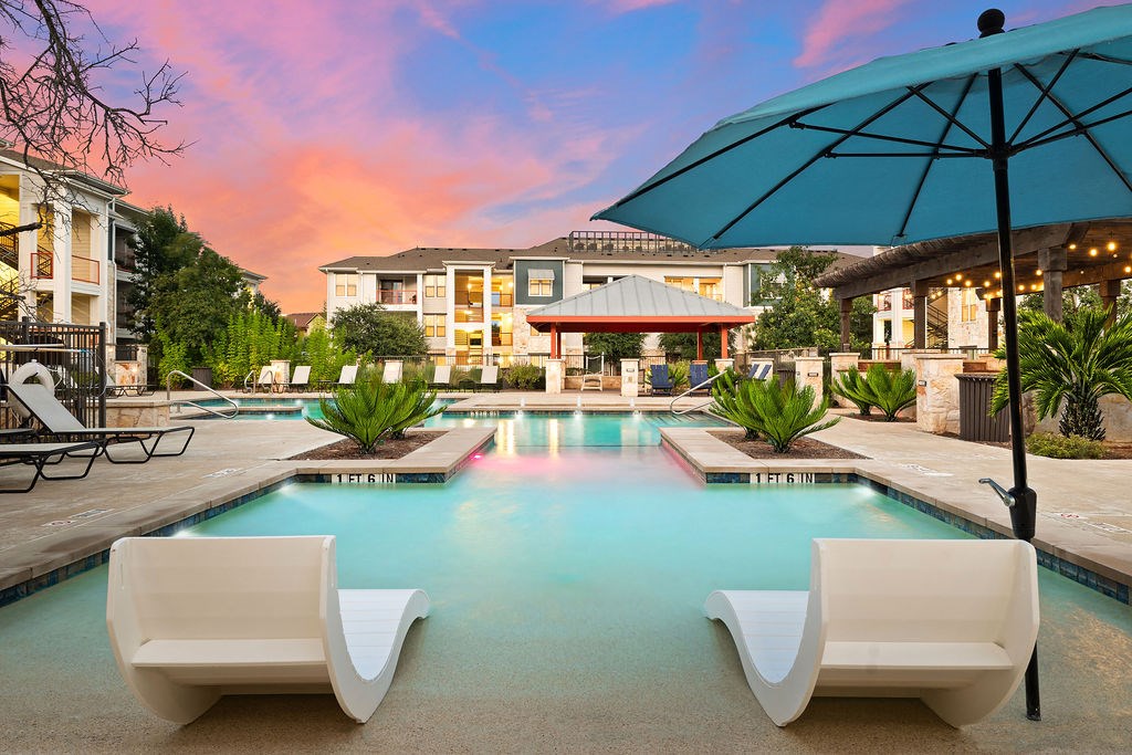 a swimming pool with two white chairs and an umbrella