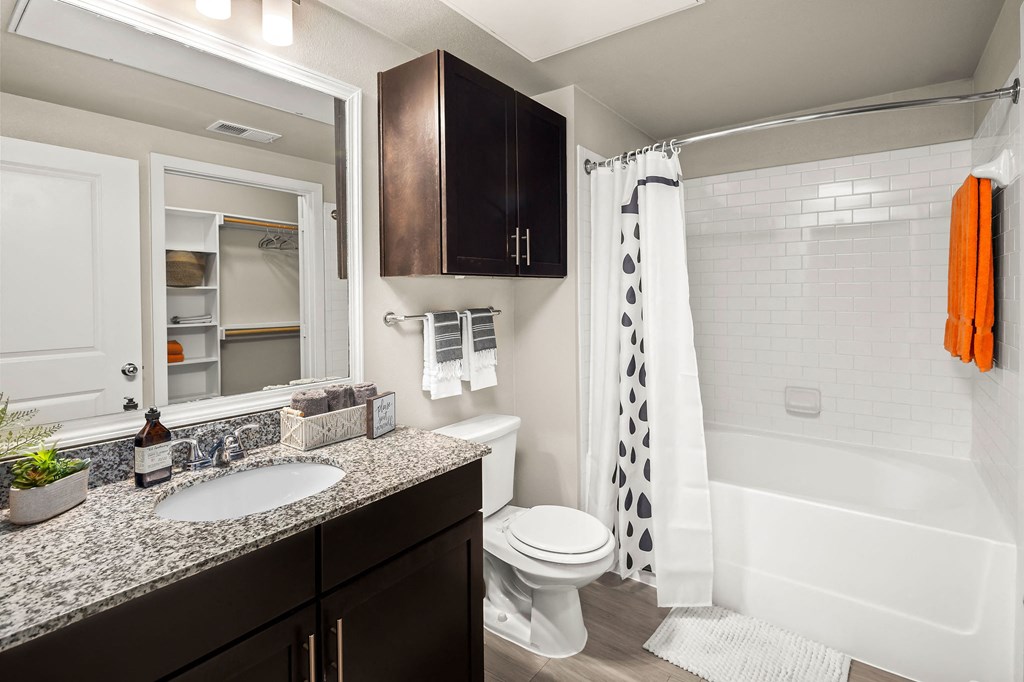 bathroom with matching countertops and cabinet above toilet. subway tile backsplash in shower/tub combo. Walk-in closet viewable from bathroom mirror.