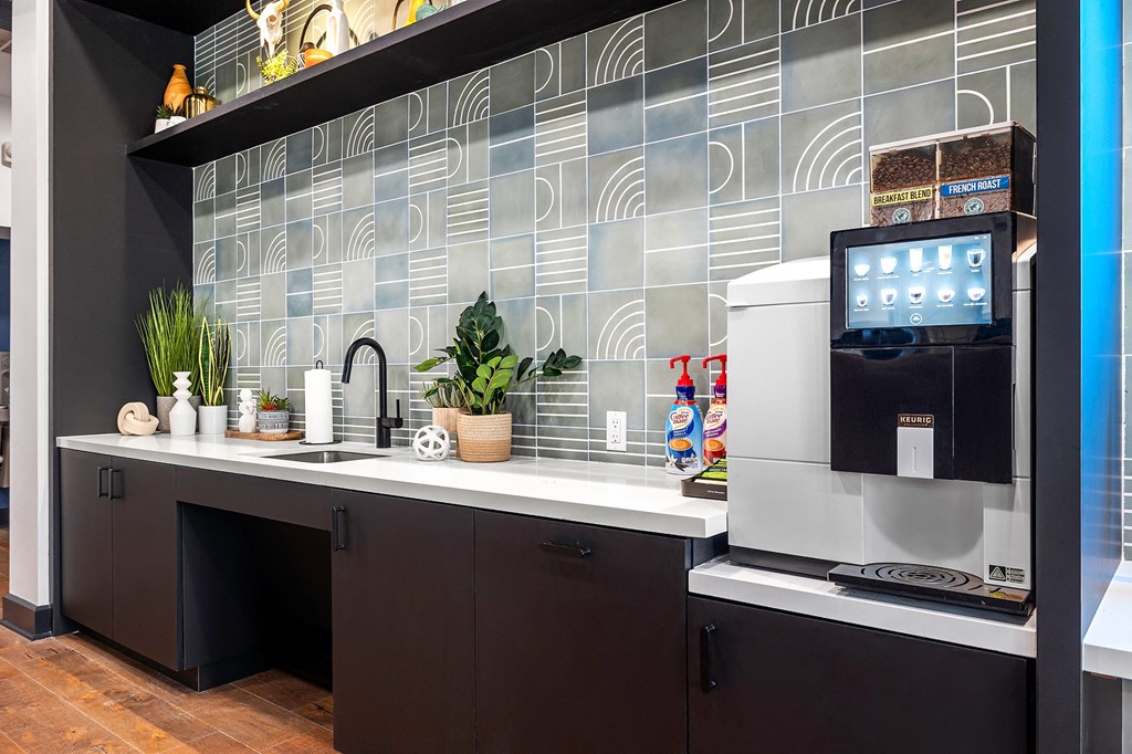 a kitchen with a sink and a coffee maker and a monitor on a counter