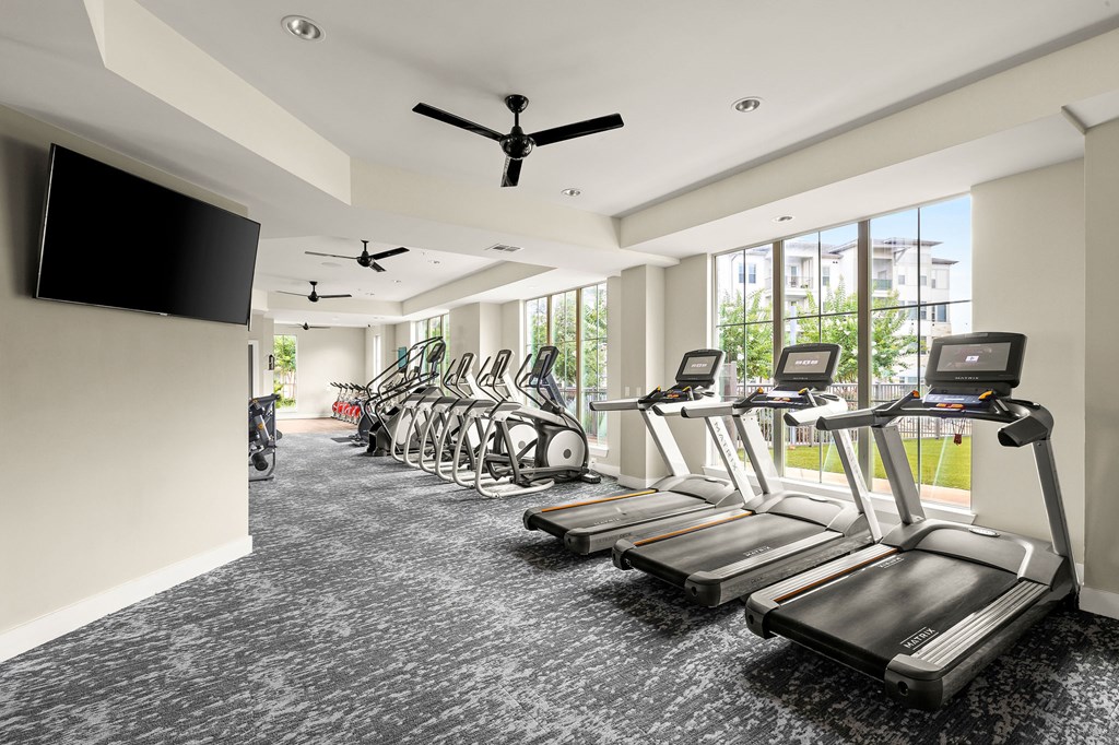 a gym with cardio machines and a tv
