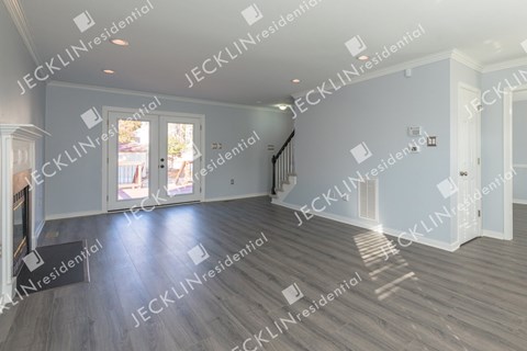 A spacious residential room with wooden flooring and a staircase.