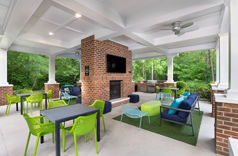 A patio with a brick fireplace and green chairs.