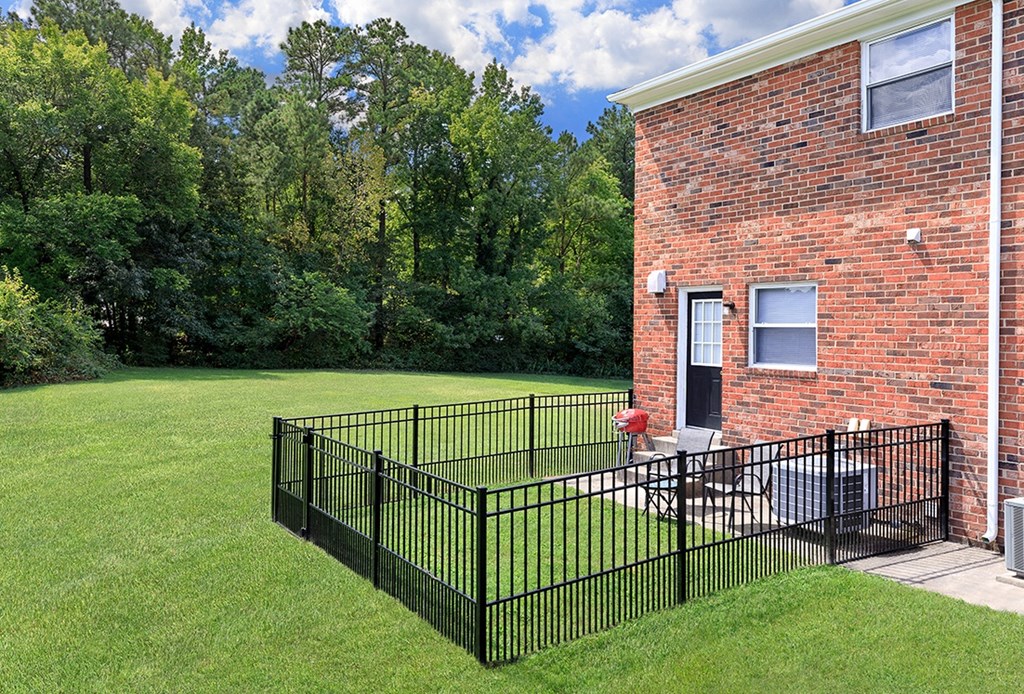 a yard with a black fence and a brick building with trees in the background