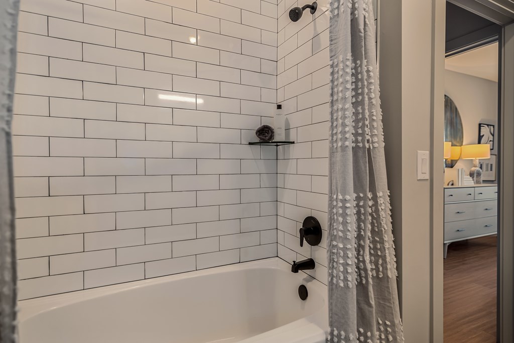A white tiled bathroom with a white bathtub and a grey shower curtain.