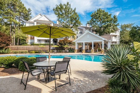 A patio with a table and chairs and a pool in the background.