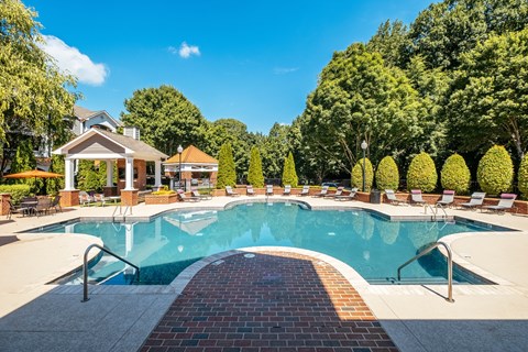 A large outdoor swimming pool surrounded by trees and a gazebo.
