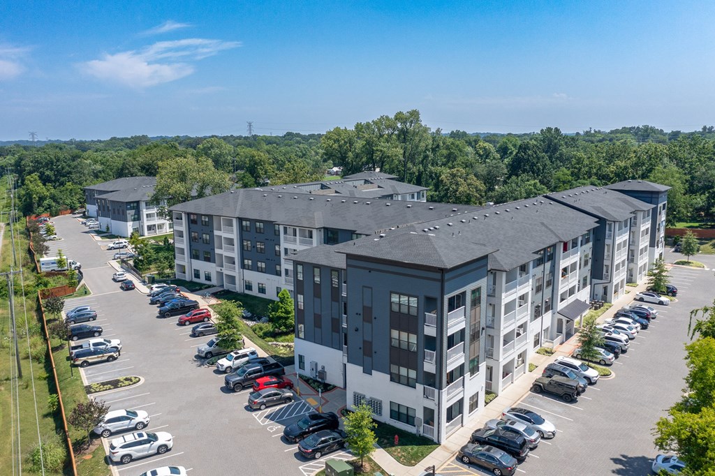 an aerial view of a large apartment complex with a parking lot and trees in the background