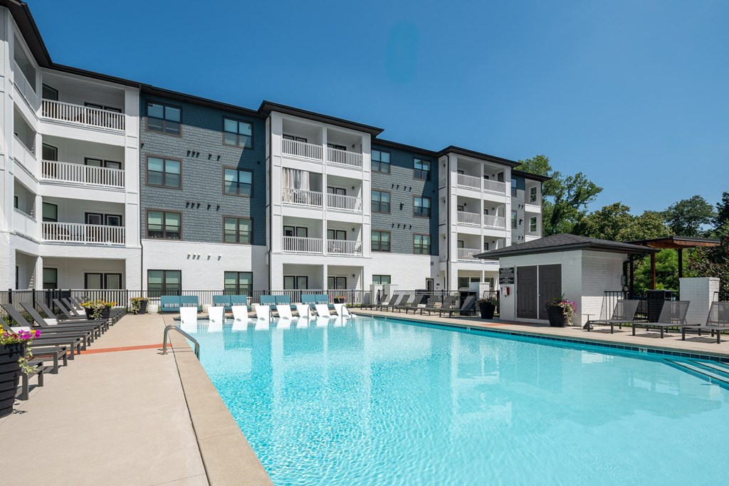a swimming pool with lounge chairs and umbrellas in front of an apartment building