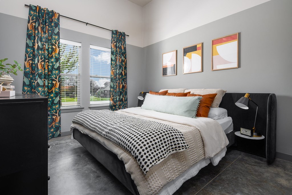 a bedroom with gray walls and a black and white bed with orange and black pillows