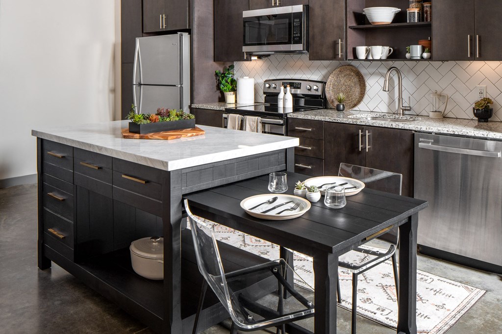 a kitchen with dark cabinets and a large island with a black table and two chairs