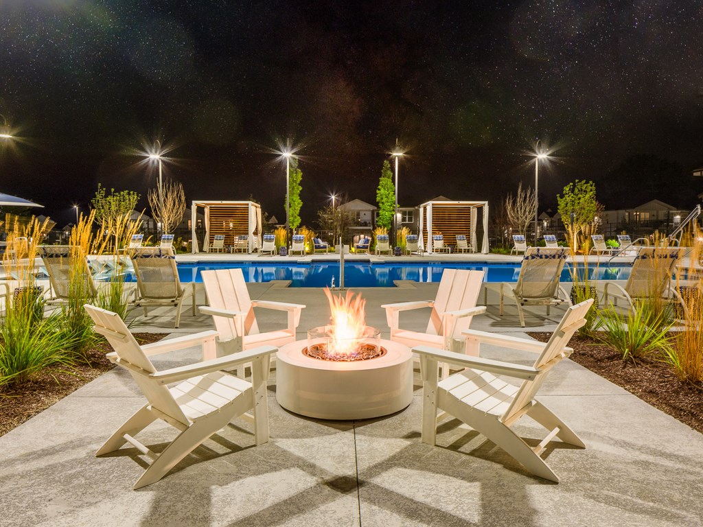 a patio with chairs around a fire pit and a pool at night