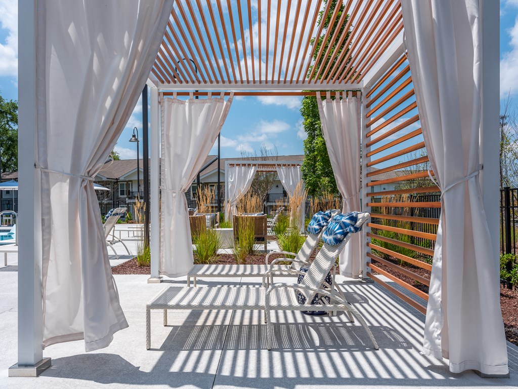 a patio with white curtains and a chair and a bench