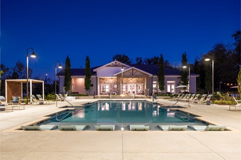 A large swimming pool in front of a building with lounge chairs around it.