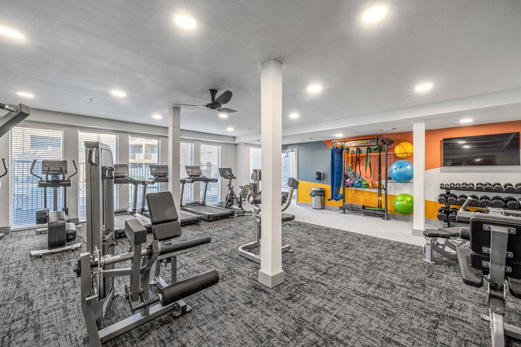 a gym with exercise equipment and a tv in a building with windows