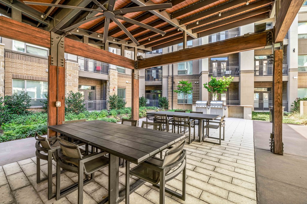 a patio with wooden tables and chairs and an apartment building in the background