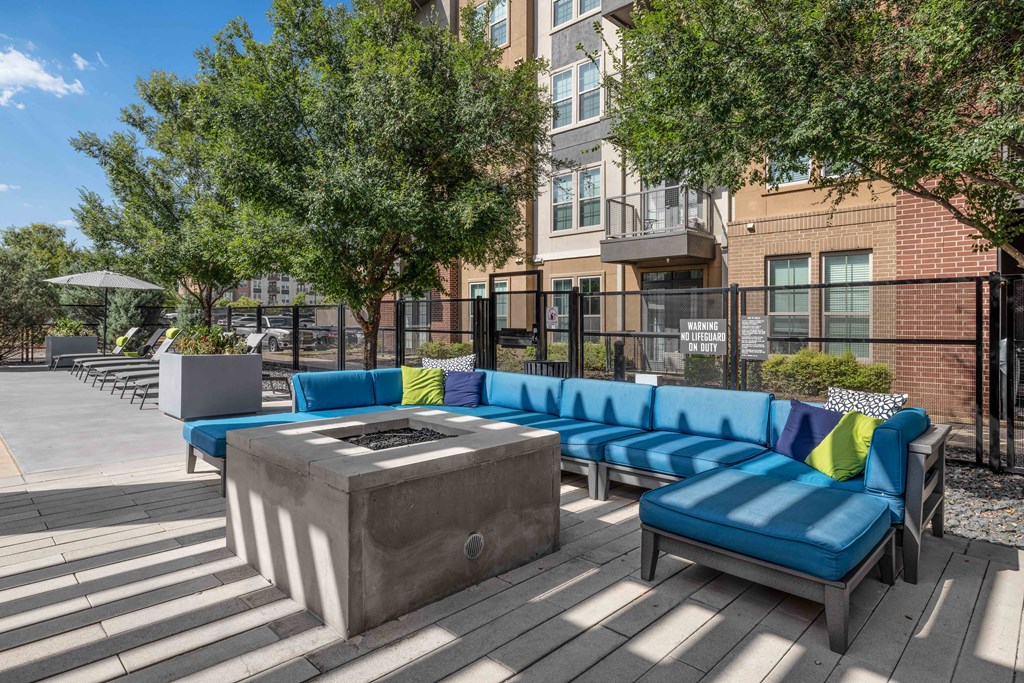 a firepit and lounge area on a wooden deck with a brick building in the background
