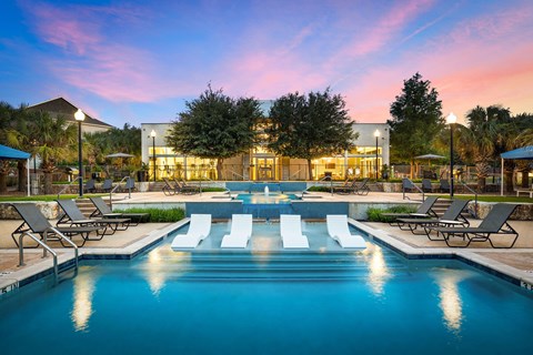 A large swimming pool in front of a building with lounge chairs around it.