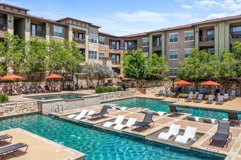 A large swimming pool with lounge chairs and umbrellas in front of apartment buildings.