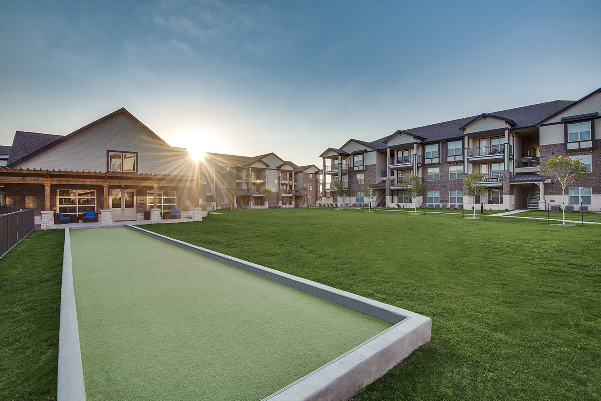 a courtyard with grass and houses with the sun setting in the background
