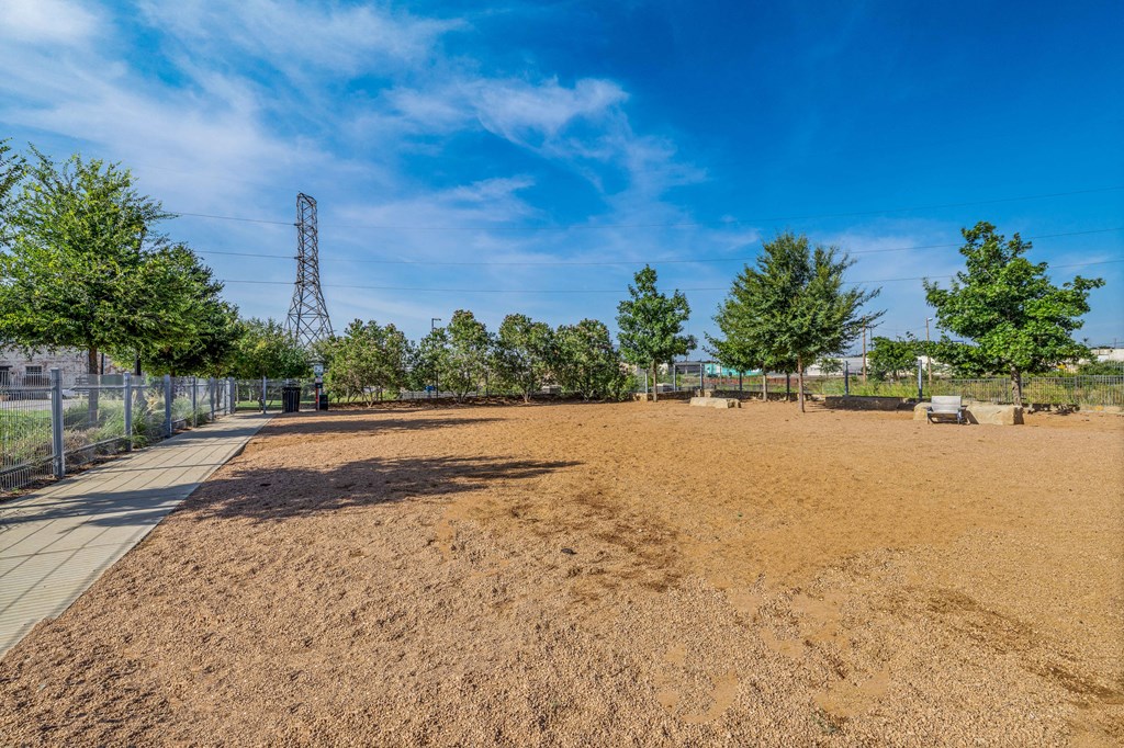 a dirt field with trees and a chain link fence