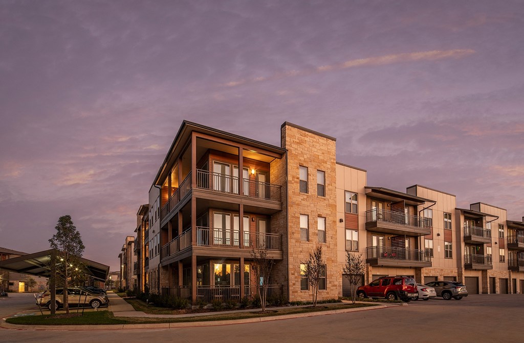 a rendering of a building at dusk with the lights on and cars parked in front of it