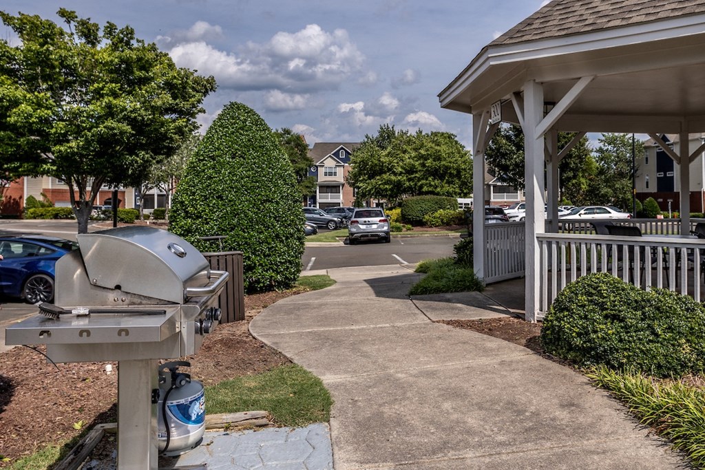 a patio with a grill and a gazebo with a parking lot in the background