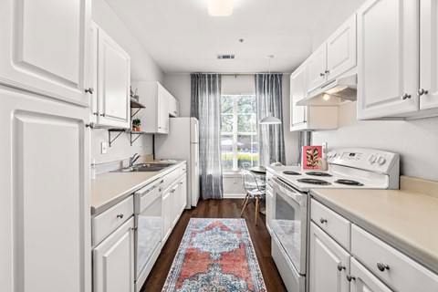 A kitchen with white cabinets and a red rug on the floor.