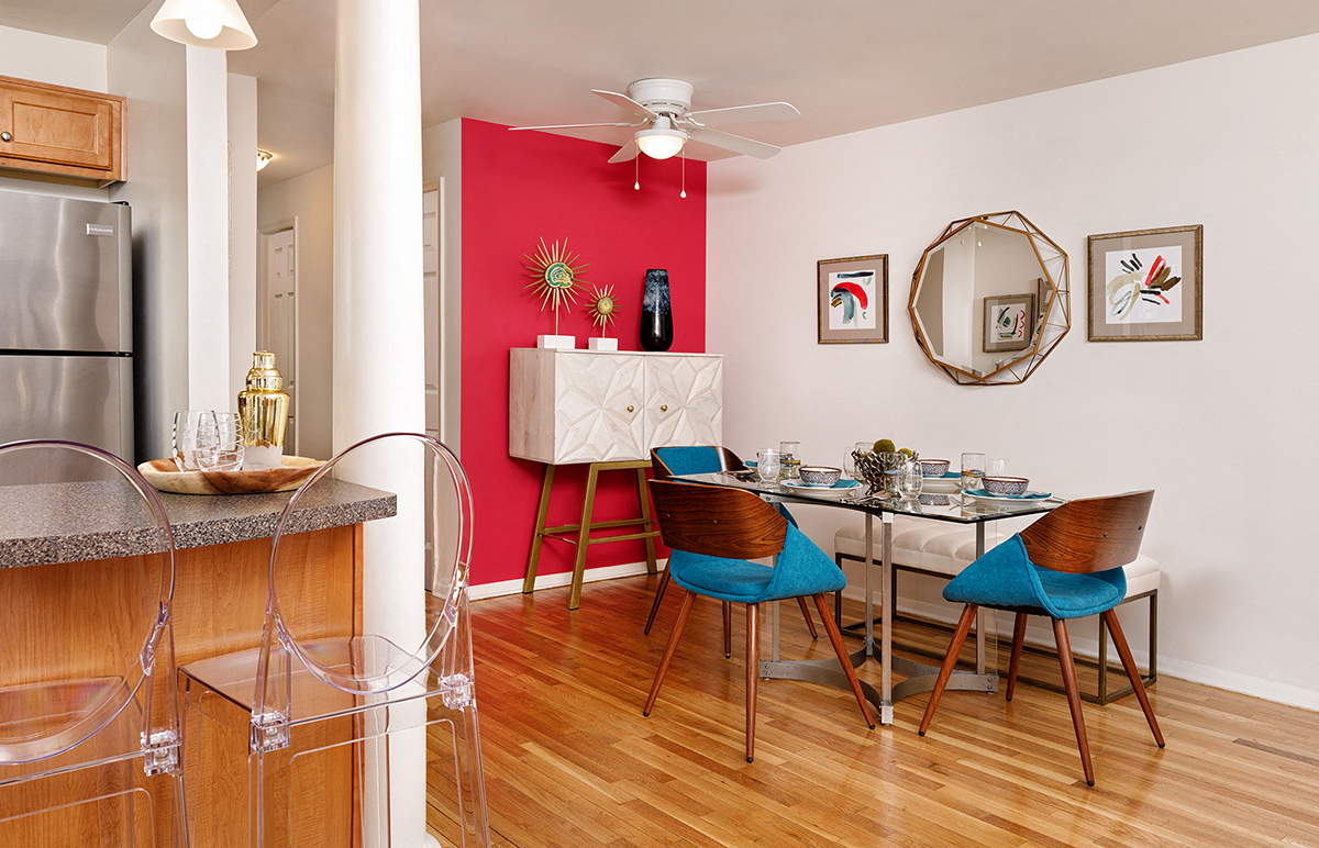 a dining room with a table and chairs and a kitchen with a red wall