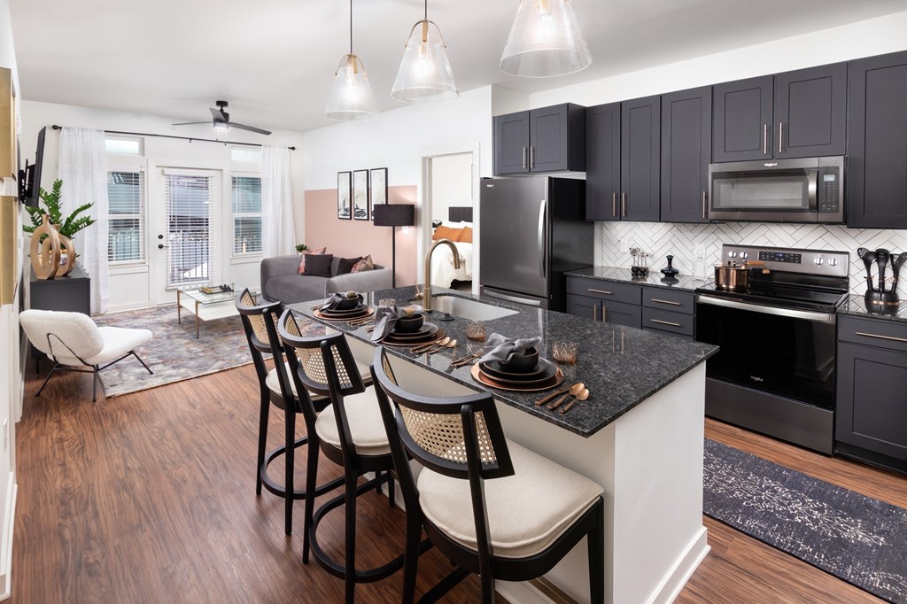 a kitchen and living room with black cabinets and a granite counter top