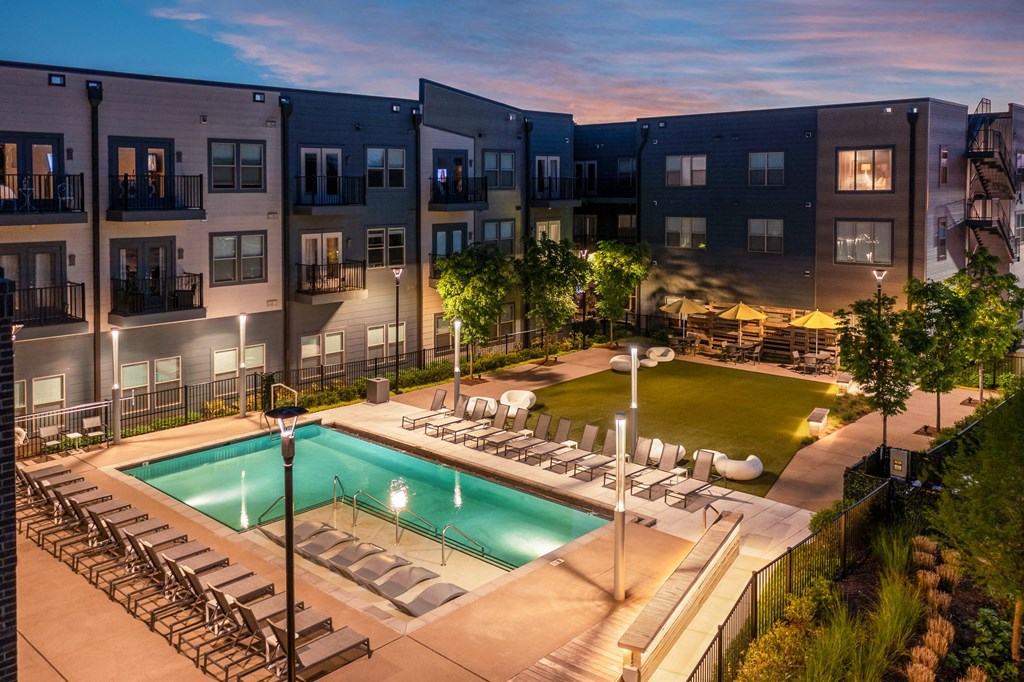 an apartment pool with lounge chairs at dusk