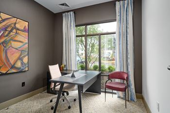 A room with a desk and a chair with a window in the background.