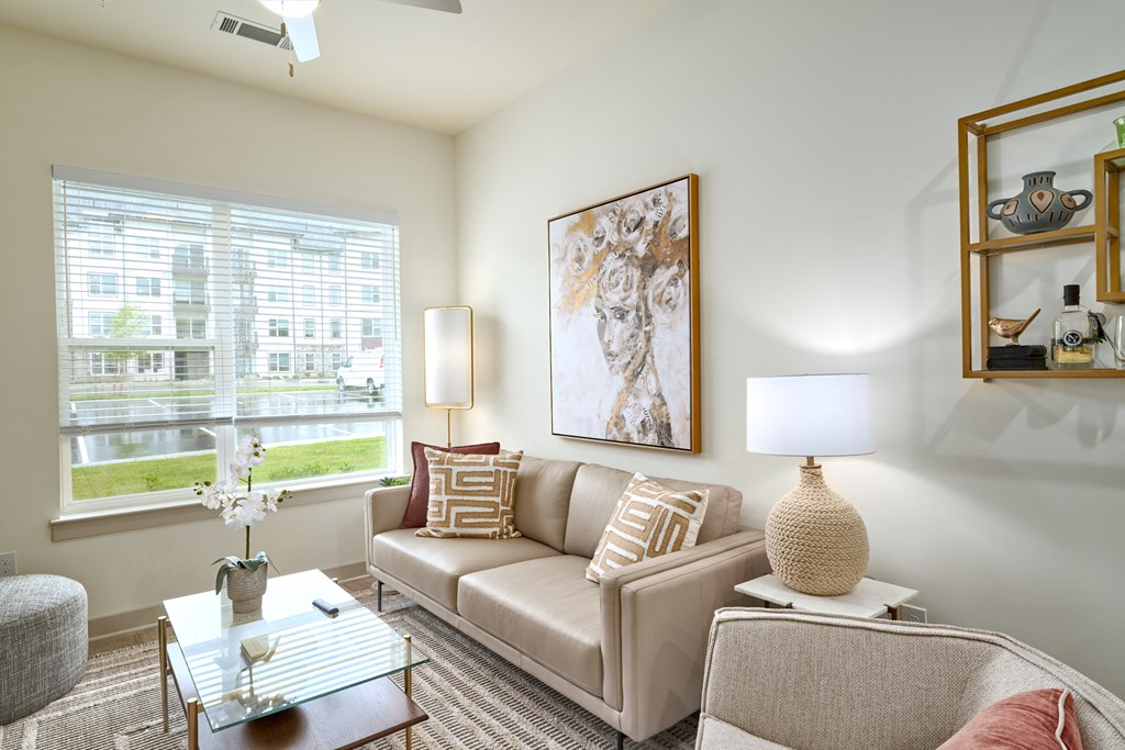 A living room with a beige couch, a glass coffee table, and a large painting on the wall.