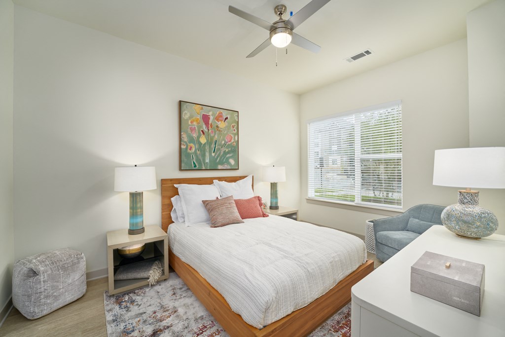 A bedroom with a large bed, a ceiling fan, and a painting on the wall.